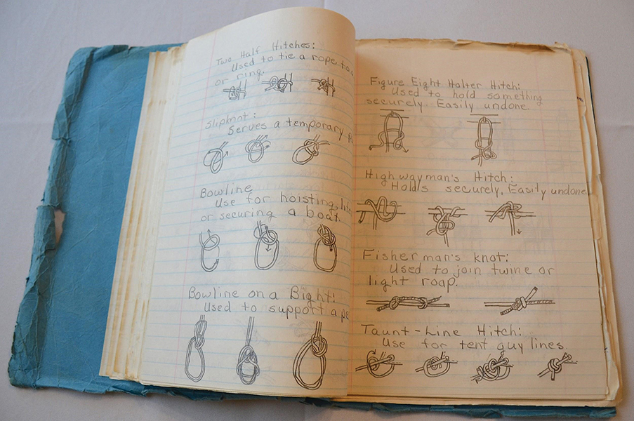 A tattered blue paper notebook open to a page of pencil drawings of different kinds of knots, including bowline, highwayman’s hitch, fisherman’s knot, and taut-line hitch.