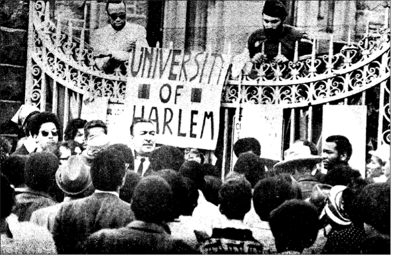 Small crowd in front of CCNY gates on which a banner reading University of Harlem hangs.