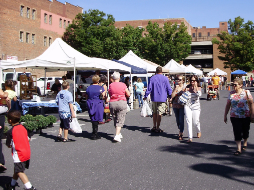 Market goers walking outside by pop-up tents.