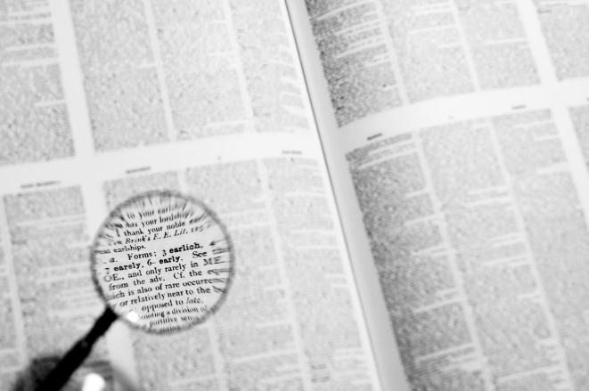 Photograph: a magnifying glass looking across a reference book. Vladuchick, Paul. Investigation, 2010. Flickr, https://flic.kr/p/8rQaXM.