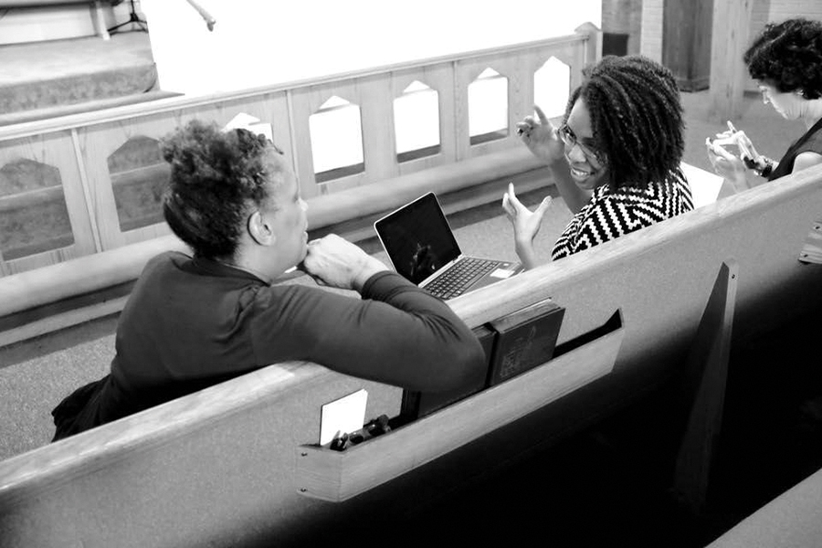 Murrain and participant are sitting on a church pew while they have a discussion. Murrain has her laptop in her lap.