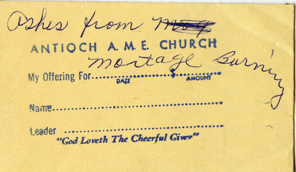 A close-up photograph of the envelope holding the ashes from the mortgage burning ceremony. The envelope is an old collections envelope with a stamp for date, name, and leader, with the words ‘God Loveth The Cheerful Giver.