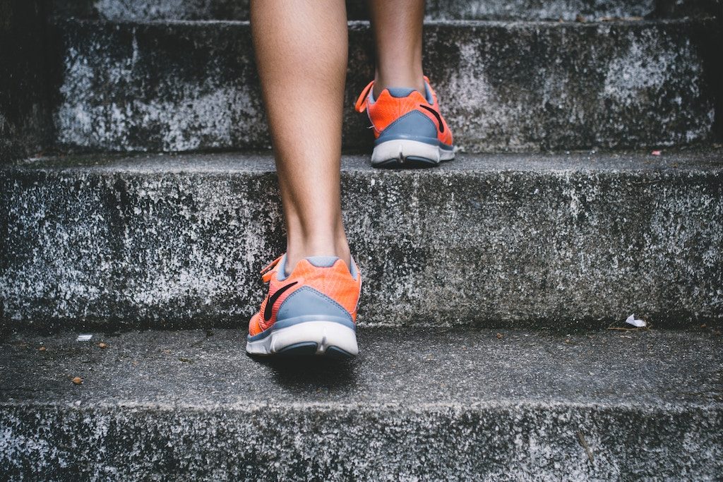 Feet in tennis shoes walking up cement stairs.