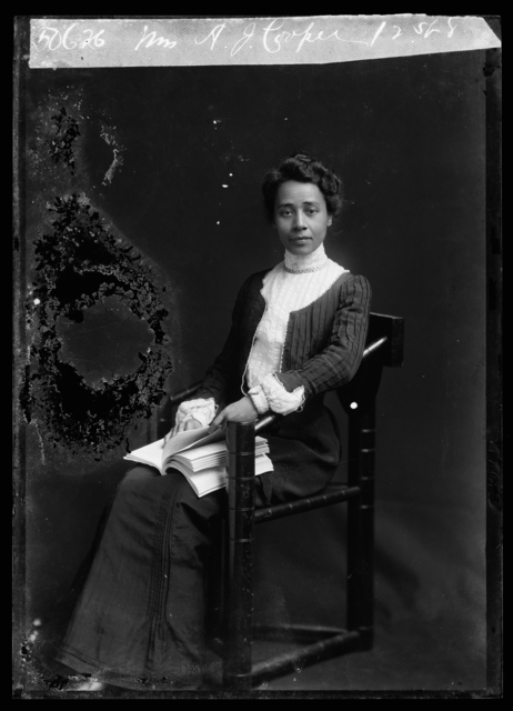 A portrait of Dr. Anna Julia Cooper seated in a chair with a book in her lap. She appears refined and confident while looking directly into the camera with a slight self-assured smirk.