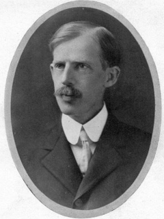 An oval-shaped, grayscale photo portrait of Fayette A. McKenzie. He is wearing a suit and his hair is neatly parted to the side. He has a full and neatly-groomed mustache.