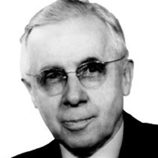 A gray-scale photo portrait of Ernest Burgess wearing a suit and tie. He is wearing classes with round lenses and he it seems he is smirking slightly. He has short-cut and neatly-groomed gray hair. He is looking off to the left. Photo Credit: unknown, Photo Source: Wikimedia Commons