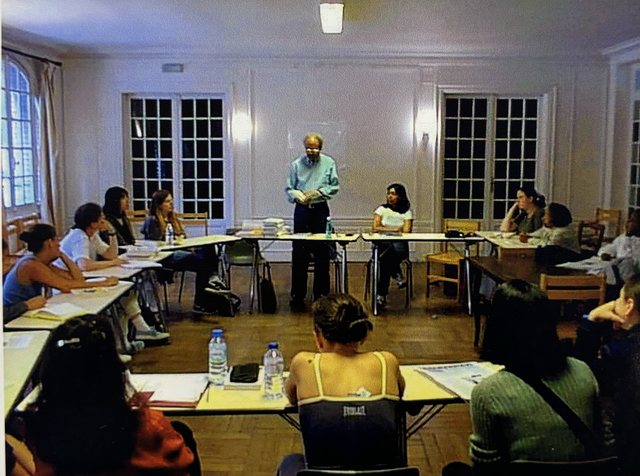 Desk are organized in a rectangle. James A. Emanuel is at the top of the rectangle. He is giving a poetry reading to Hunter College Students in Hulstrand's study abroad program 'Paris Through the Eyes of Travelers.' 
