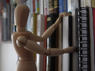 A wooden figure appears to be browsing for books in a library. 