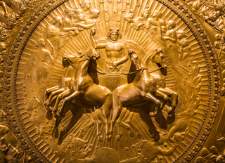 A close-up view of Flaxman's 1822 Shield of Achilles. In it, horses emerge from the shield, led by a charioteer - the sun-God, Apollo - who is surrounded by stars and other deities.  